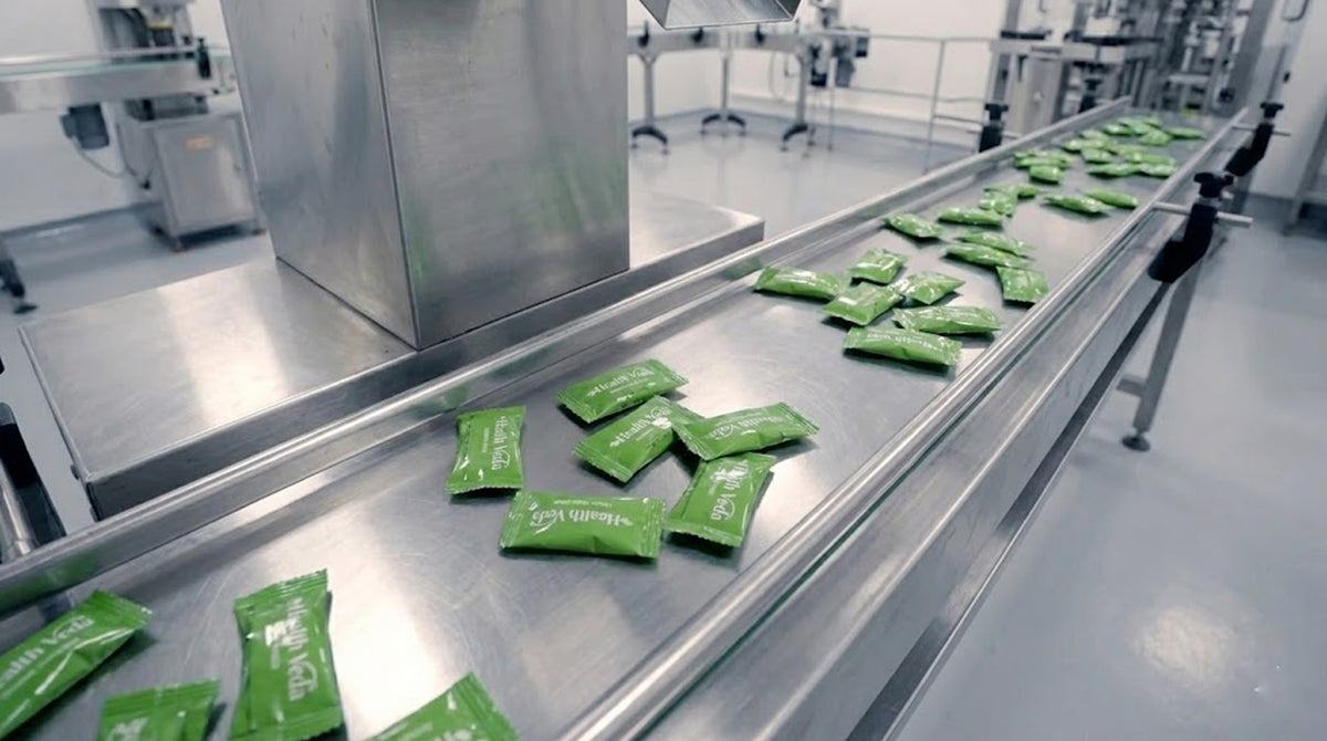 Individually wrapped HealthVeda gummies along a stainless-steel conveyor.